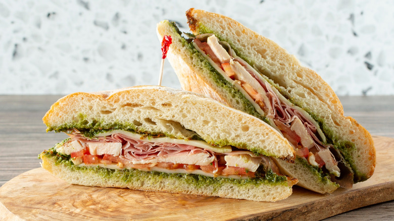 Sandwich sliced in half filled with basil pesto chicken, ham, tomato, and cheese.