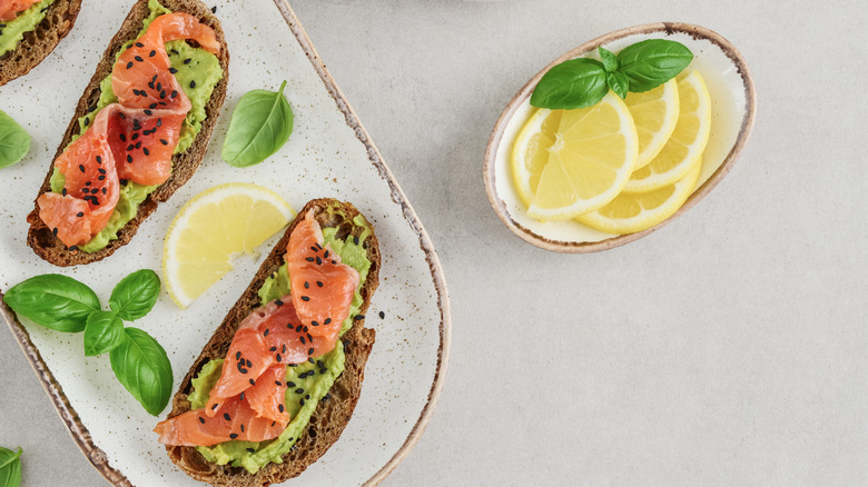 Slices of bread topped with smoked salmon and avocado, alongside a bowl of lemon slices