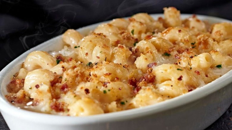 A white dish of bubbling hot mac and cheese with flecks of cheese and bacon