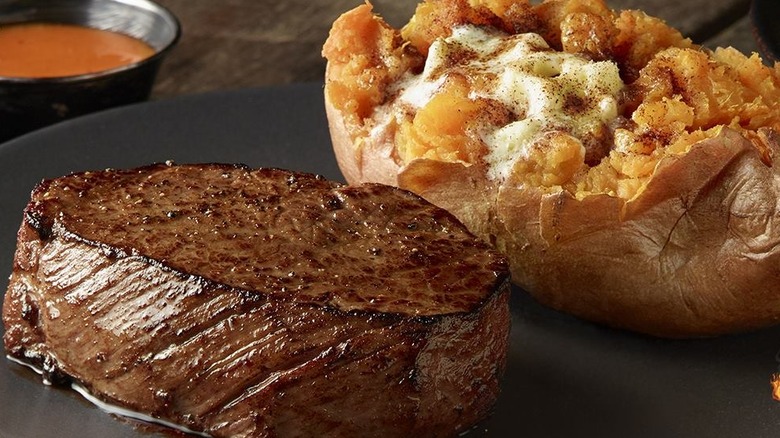 A black plate topped with a seared sirloin with a loaded jacket potato next to it