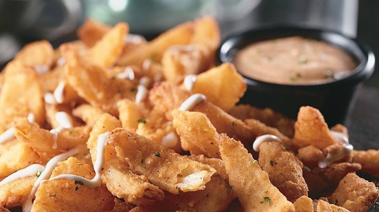 Batter fried onion pellets topped with a mayonnaise drizzle with a small bowl of creamy dip in the background