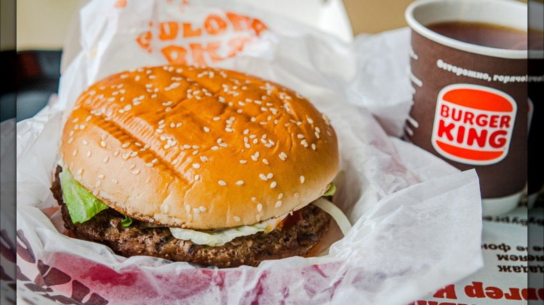 A Burger King Burger sits on a tray next to a cup of coffee