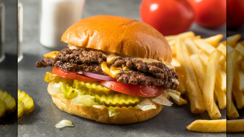 A burger surrounded by fries and ingredients sits on a surface