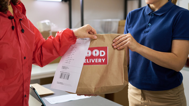 A cashier hands a customer a bag with receipt attached