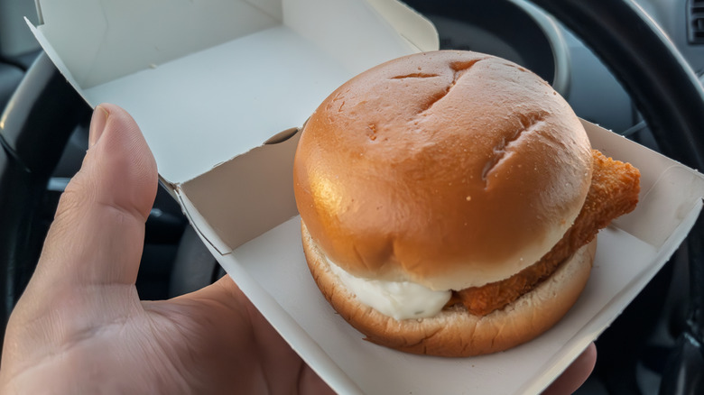 A person's hand holding a filet-o-fish in small takeout box in their car