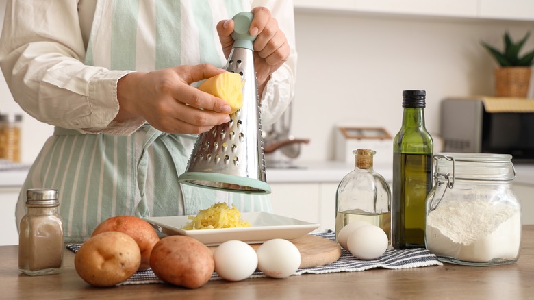 a woman grating potatoes in a kitchen with eggs, oil, and flour on the table