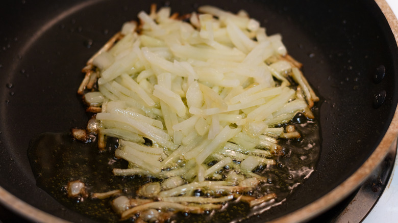 Fresh shredded, hashbrown potatoes frying in a pan with oil on the stove