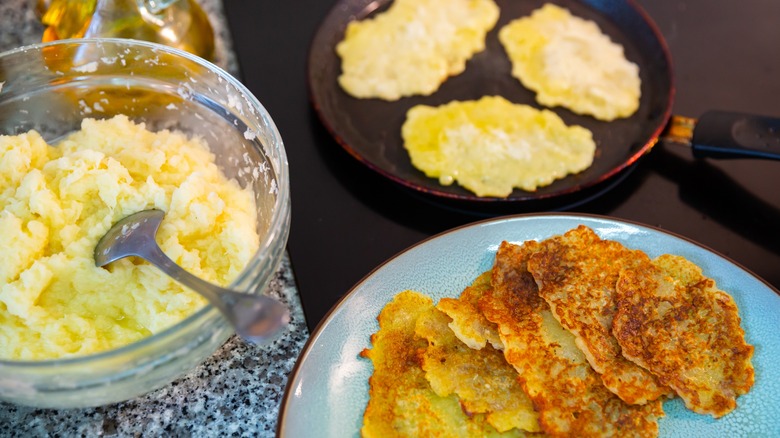 cooking process of hash browns wiht some cooked hashbrowns on a plate, some on a pan and grated potatoes in a bowl with a spoon