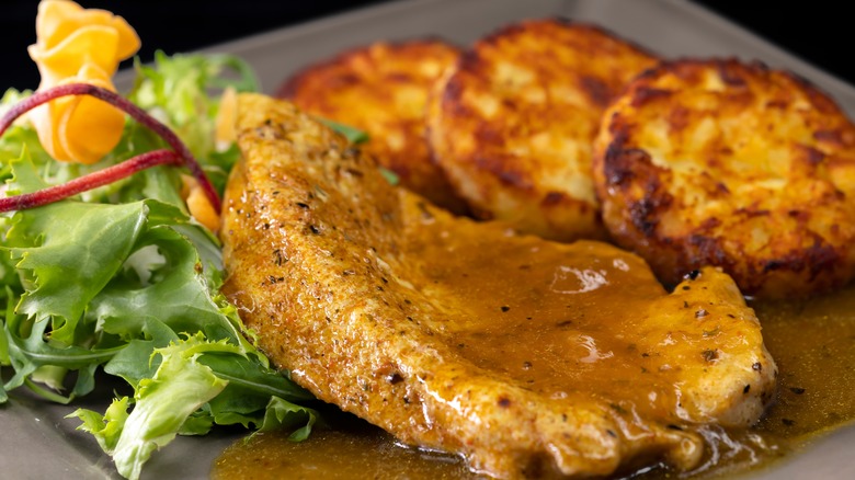 poultry meat with sauce served with hash browns and salad