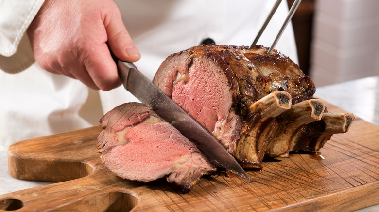 Bone-in roast prime rib being sliced on a cutting board
