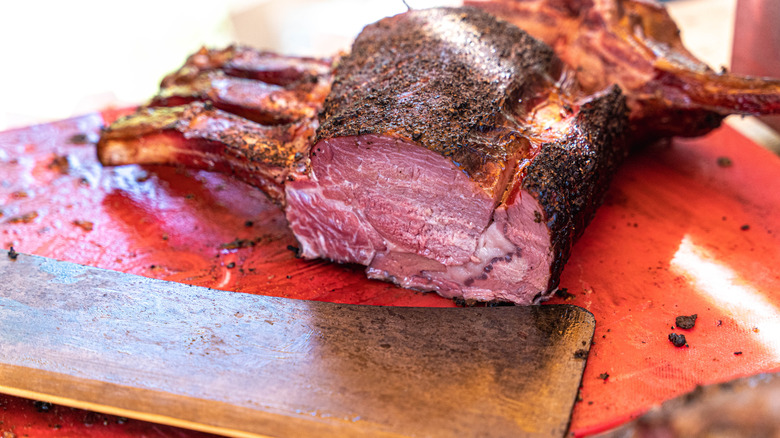 Juicy sliced smoked prime rib roast with a cleaver resting on a red cutting board
