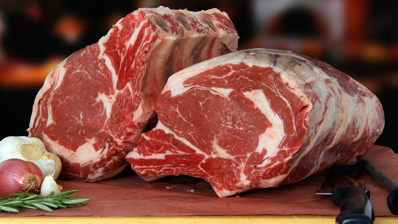 Raw prime rib roasts on a board with garlic and herbs