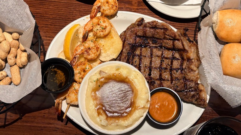 Sirloin steak, shrimp, and mashed potatoes from Texas Roadhouse, next to bowls of rolls and nuts