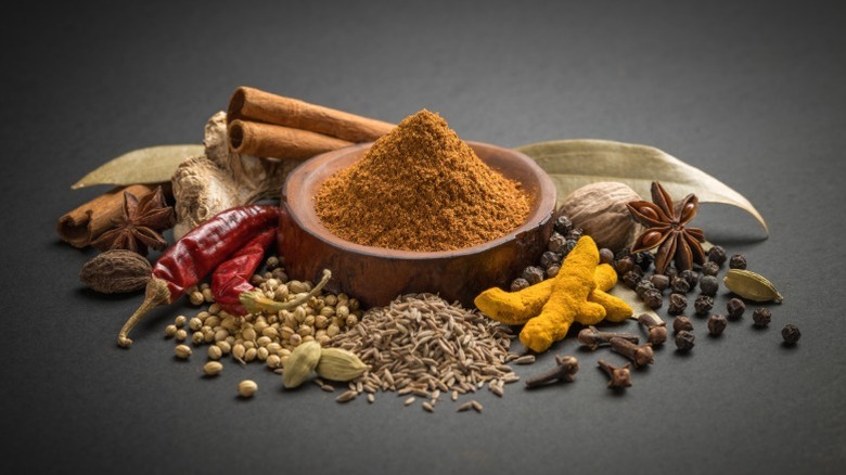 A bowl of garam masala with herbs and peppers surrounding it