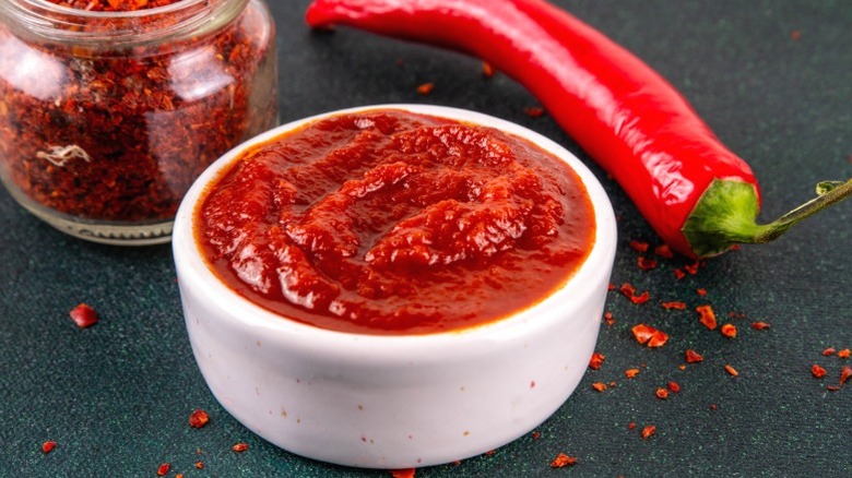 A white bowl of gochujang paste next to a pepper.