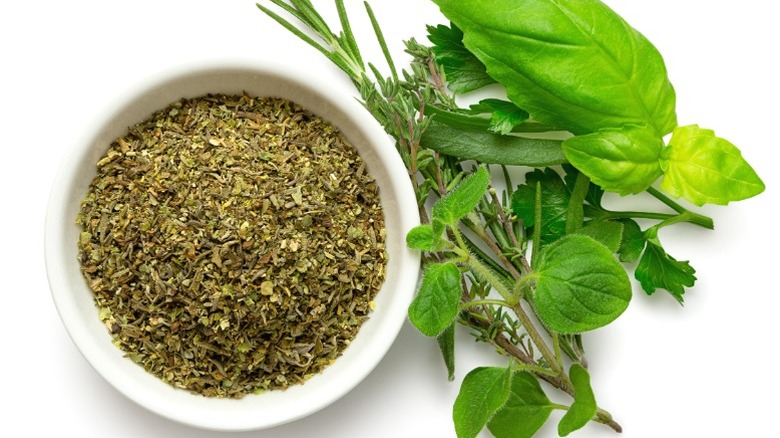 A bowl of herbes de provence next to herbs on the stem.