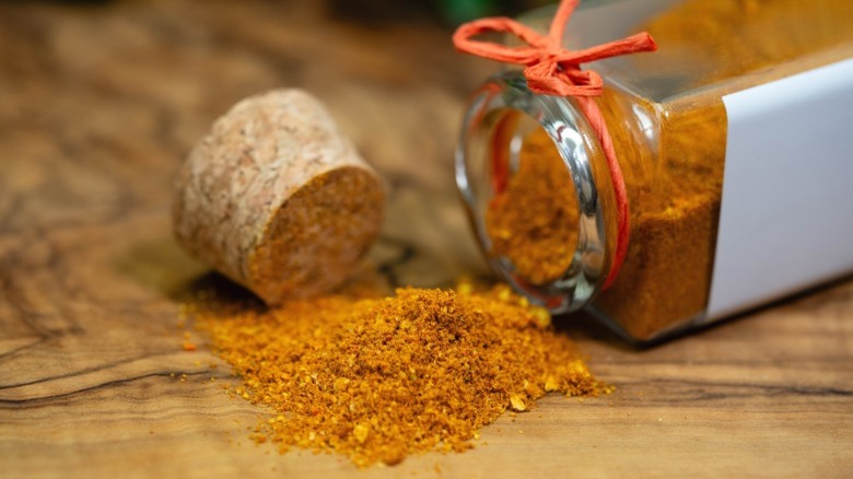A jar of ras el hanout, tipped over with contents spilling on wooden surface