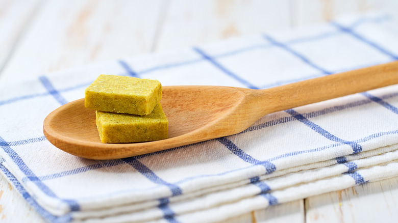 Bouillon cubes on a wooden spoon on a checkered dish cloth