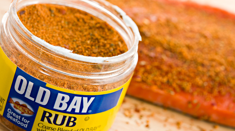 Plastic Jar of Old Bay Rub with with a piece of spice-rubbed salmon out of focus in the background