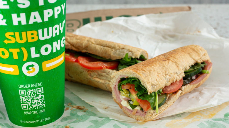An unwrapped Subway footlong sandwich with a drink
