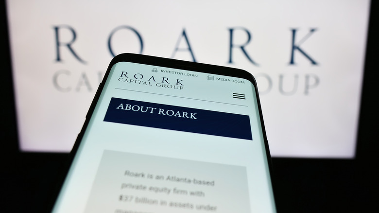 Mobile website of Roark Capital on phone in front of Roark Capital logo on computer screen