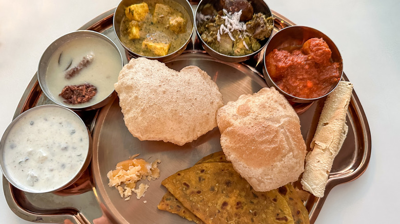 A steel platter of small bowls of curries with Indian flatbreads