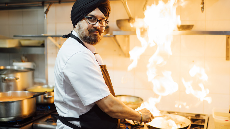 An Indian chef looking at the camera while he cooks at a stove