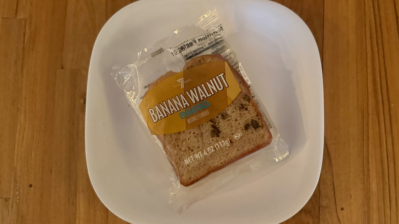 A slice of 7-Select Banana walnut bread in a plastic wrapper on square white plate