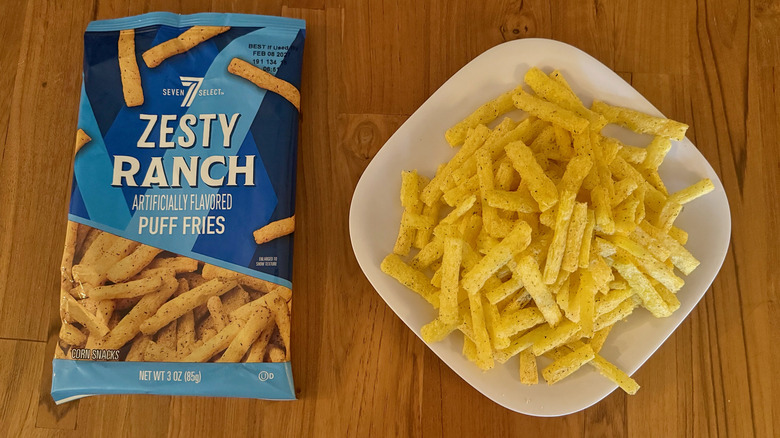 A blue bag of 7-Select Zesty Ranch Puff Fries next to a square white plate piled with fries