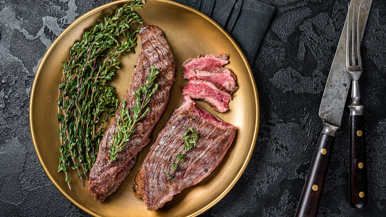 Bavette steak served on a gold plate with rosemary, alongside cutlery