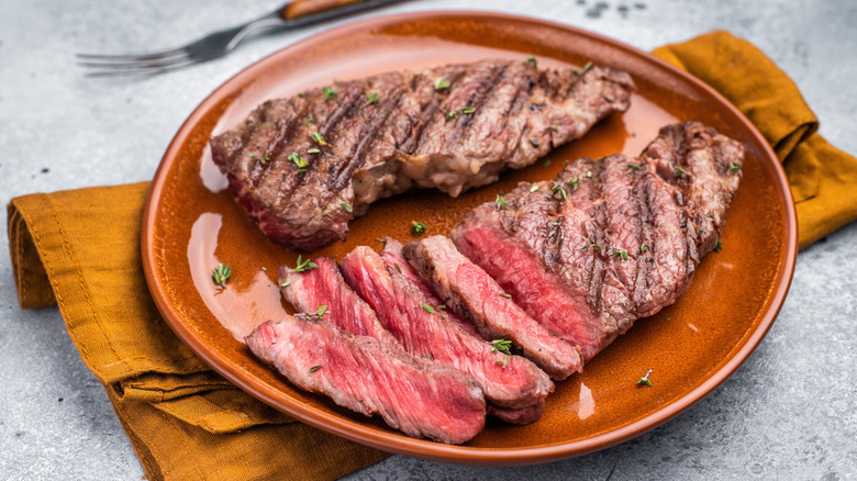 Two grilled flat iron steaks on a plate, one sliced
