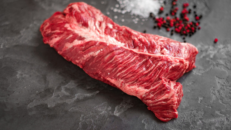 Raw hanger steak with peppercorns in the background