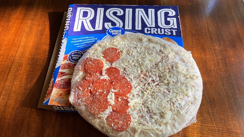 Frozen pizza with one side piled with pepperoni atop a pizza box with the words "RISING CRUST" in large letters across the top.box.