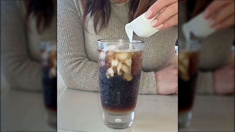 Creamer is being poured into a glass of Pepsi with ice and lime juice to create a dirty Pepsi