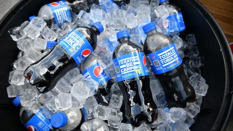 Bottles of Pepsi are piled in a black bin, filled with ice.