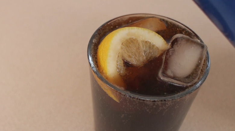A glass of Pepsi with ice cubes, and a wedge of lemon floating in it.