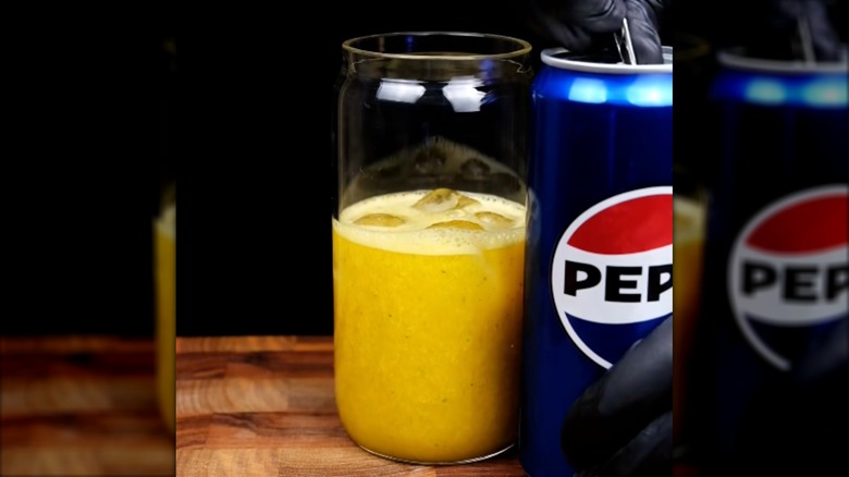 Hand cracks open a can of Pepsi next to a glass of freshly squeezed orange juice with ice