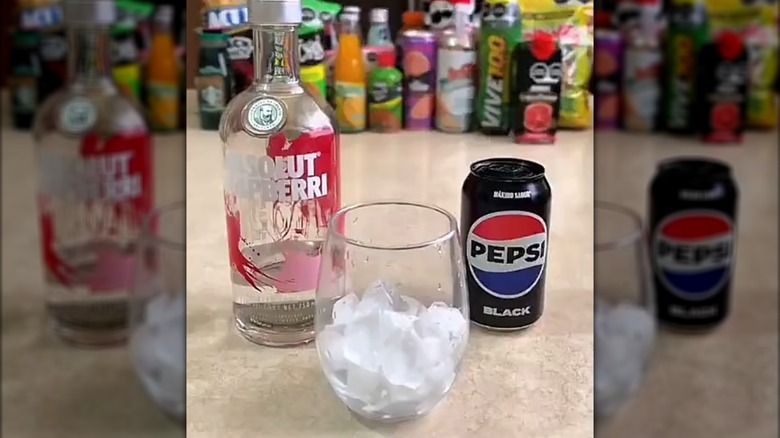 A glass of ice between a can of Pepsi and a bottle of Absolut vodka