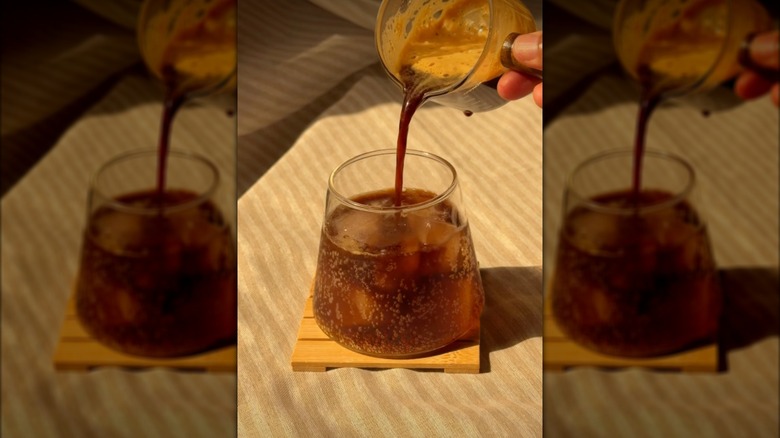 Hand pours measuring glass of espresso into a bubbly glass of Pepsi and ice
