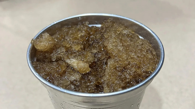 A closeup of the top of a metal glass filled with a Pepsi slushy.