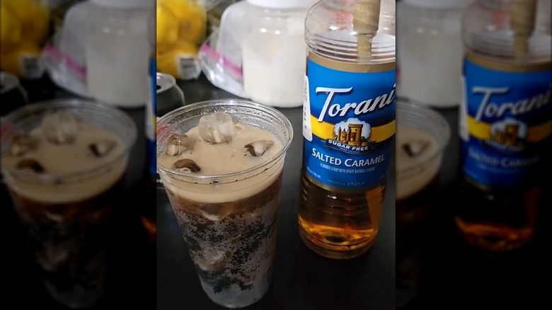 Plastic glass of pepsi with ice next to Torani bottle of salted caramel syrup
