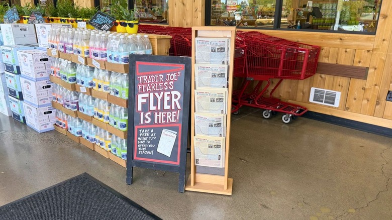 Sign advertising Trader Joe's frequent flyer next to stand of flyers and shopping carts in store entrance