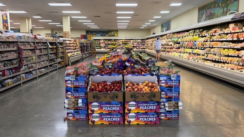 Wide shopping aisle at Trader Joe's with produce in the center and refrigerated rows of cheese to the side