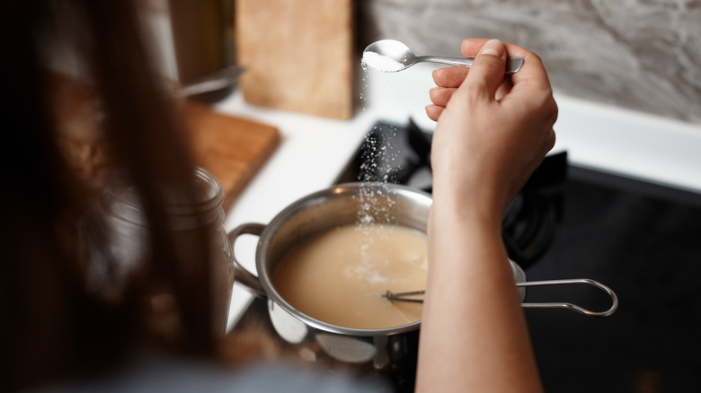 Woman adding sugar while cooking soup