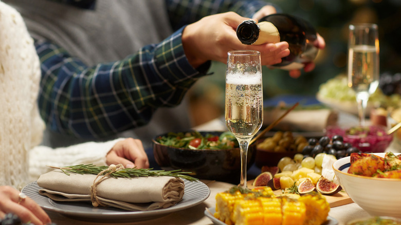 Man pouring sparkling champagne into glass helping female friend while sitting at dining table