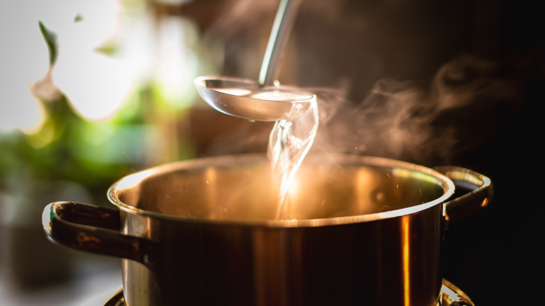 A boiling pot steams up as a restaurant chef uses a ladle to stir soup in a cooking pot