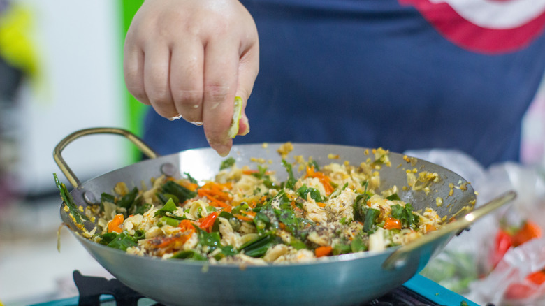 Close-up of a hand squeezing fresh lime juice over a wok of stir-fried chicken and vegetables