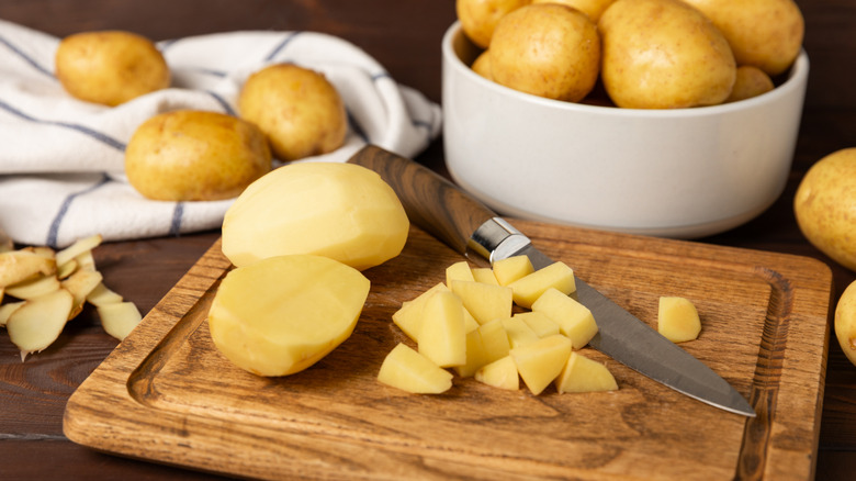 Raw potatoes and knife on a wooden background