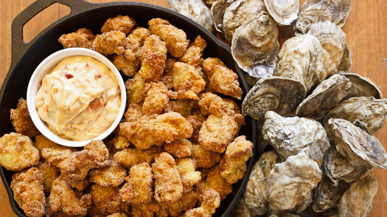 Fried oysters in a cast iron pan with a ramekin of sauce next to oyster shells