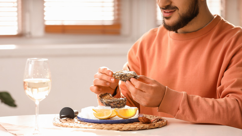 Man in peach sweatshirt holding a raw oyster over a plate of ice and lemon wedges, and smiling